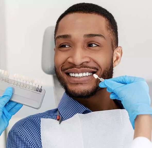 Man sitting in chair with shade tool held to teeth to match colour.